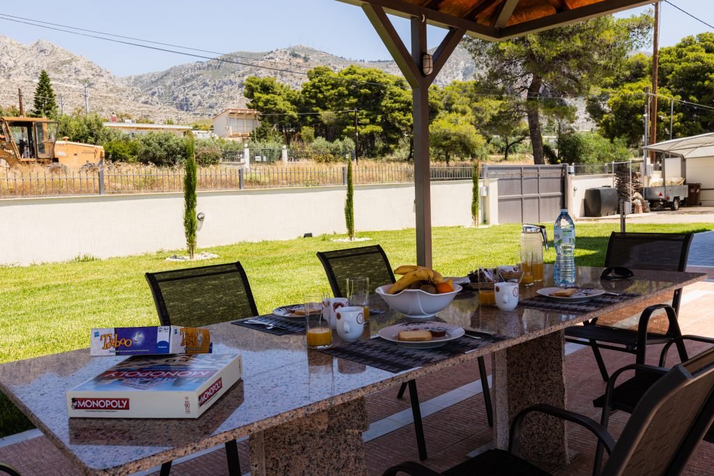 Εξωτερική τραπεζαρία στη Villa Memories στην Κινέτα με μεγάλο τραπέζι και πράσινο κήπο