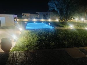 Η φωταγωγημένη πισίνα της Villa Memories στην Κινέτα το βράδυ περιτριγυρισμένη από δέντρα και γκαζόν