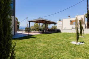 Κήπος της Villa Memories στην Κινέτα με γκαζόν και στεγασμένη εξωτερική τραπεζαρία