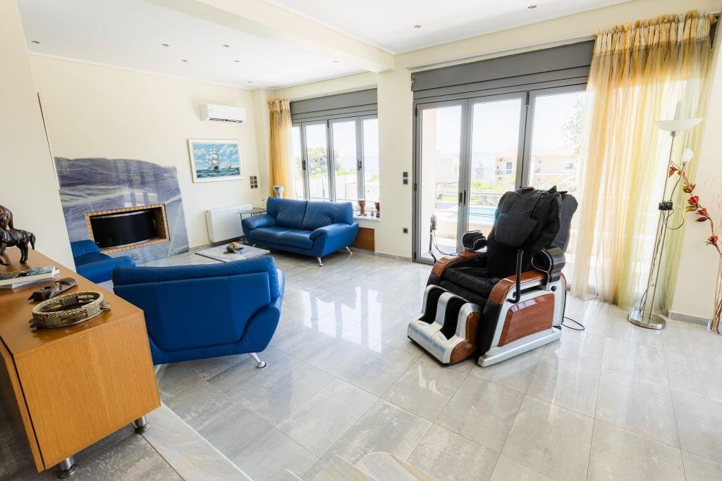 Ευρύχωρο σαλόνι στη Villa Memories στην Κινέτα με τζάκι, καναπέδες και θέα προς την πισίνα