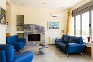 Καθιστικό της Villa Memories στην Κινέτα με μπλε καναπέδες και μοντέρνο τζάκι