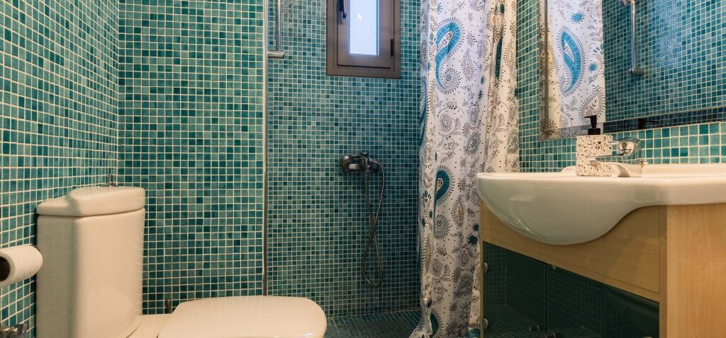 Μπάνιο με επένδυση μπλε ψηφίδας, ντουζιέρα και ξύλινο έπιπλο νιπτήρα στη Villa Memories