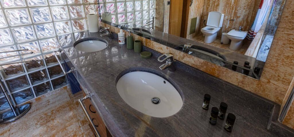 Μεγάλος μαρμάρινος πάγκος μπάνιου με δύο νιπτήρες, καθρέπτη και είδη περιποίησης στη Villa Memories