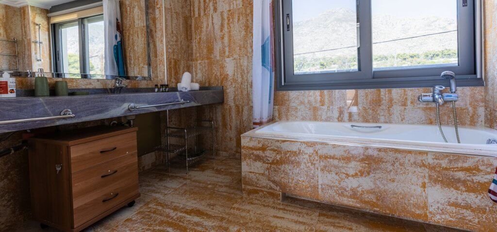 Μπάνιο στη Villa Memories με μαρμάρινη επένδυση, μεγάλη μπανιέρα και παράθυρο με θέα στο τοπίο της Κινέτας